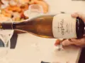 Eine Hand gießt einen **fumé wein** aus einer Flasche in ein Glas. Im Hintergrund ist eine Platte mit Speisen zu sehen.