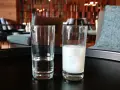 Zwei Gläser auf einem Tisch: eines mit klarem Wasser, das andere mit milchigem Ouzo. Ein Vergleich zwischen Raki und Ouzo.