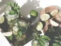 Erfrischendes Mojito Rezept: Gläser mit Eis, Minze und Limettenspalten auf einem Tablett. Frische Limetten und Minze liegen daneben.