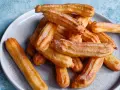 Goldbraune Churros, frisch aus dem Airfryer, mit Zucker bestreut auf einem grauen Teller.