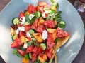 Erfrischender Melonensalat mit Mozzarella, Gurke und Basilikum auf einem grauen Teller.