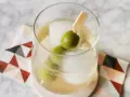 Erfrischender Italicus Spritz mit Eiswürfeln und Oliven auf einem gemusterten Untersetzer.