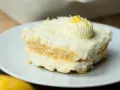 Ein Stück cremiges Limoncello Tiramisu, garniert mit Zitronenzesten und einem Tupfer Sahne, auf einem weißen Teller.