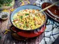Herzhafte Nudelpfanne mit Würstchen und Erbsen, perfekt für schnelle Abendbrot Rezepte. Ein Holzlöffel liegt bereit.