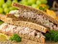 Zwei Tramezzini mit Thunfischsalat, Sellerie und Zwiebeln auf Vollkorntoast. Dazu Trauben, Zitrone und Petersilie. Perfekt für schnelle Tramezzini Rezepte.