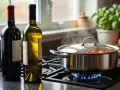 Zwei Flaschen Wein, rot und weiß, stehen neben einem Topf, in dem etwas auf dem Herd köchelt. Die Frage: welcher Wein zum Kochen?