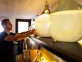 Mann sortiert Flaschen für die Gin-Lagerung. Daneben stehen Fässer und große Glasballons.