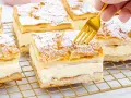 Ein goldener Löffel sticht in ein Stück polnischer Puddingkuchen, bestäubt mit Puderzucker.