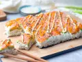 Rechteckiges Sushi mit Lachs und Avocado, verziert mit Mayonnaise und Sesam. Perfekt, um Sushi selber machen zu lernen!