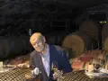 Ein Mann mit Brille hält ein Glas Wein in einem Weinkeller. Die Fässer im Hintergrund und der Wein lassen an Wein und Musik denken.