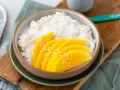 Schüssel mit cremigem **sticky rice** und saftigen Mangoscheiben, bestreut mit Sesam. Ein köstlicher Genuss!