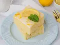Zwei Stücke griechischer Zitronenkuchen mit Joghurt, garniert mit Zitronenscheibe und Minze, auf einem hellblauen Teller.