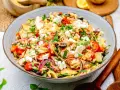 Bunter Kritharaki Salat mit Feta, Tomaten, Gurken, roten Zwiebeln und Oliven, garniert mit Petersilie. Ein köstlicher mediterraner Genuss.