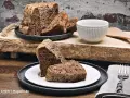 Zwei Stücke eines rustikalen, dunklen Diabetiker Kuchens auf einem Teller, daneben eine Schüssel und ein Messer.