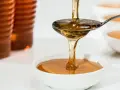 Goldener Sirup fließt von einem Löffel in eine Schüssel. Ob es sich um Agavendicksaft oder Honig handelt, ist schwer zu sagen.