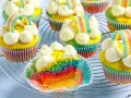 Bunte regenbogen muffins mit weißem Frosting und Gummibärchen-Regenbogen-Deko auf einem Gitter.