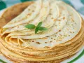 Ein Stapel goldbrauner Pfannkuchen, wie nach Omas Pfannkuchen Rezept, mit einem Minzblatt garniert.
