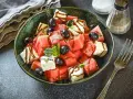 Erfrischender Melone Feta Salat mit schwarzen Oliven und Minze, beträufelt mit Balsamico-Glasur.