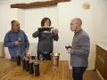 Weinprobe: Eine Frau schenkt Wein ein, während zwei Männer zuschauen. Auf dem Tisch stehen Flaschen für die Assemblage.