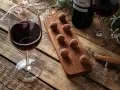 Ein Glas Rotwein und Schokolade-Trüffel auf einem Holzbrett, daneben eine Flasche Rotwein und Lichterketten.