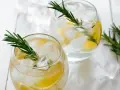 Zwei erfrischende Gin mit Zitrone und Rosmarin, serviert mit Eiswürfeln auf weißem Holz.