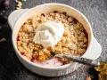 Ein warmer Zwetschgen Crumble mit Haferflocken, gekrönt von einem Klecks Sahne. Ein Löffel hebt die süße Frucht hervor.