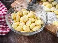 Frisch gemachte Gnocchi in einer Schüssel, bereit zum Kochen. Auf dem Holzbrett liegen weitere Gnocchi, die zeigen, wie einfach es ist, Gnocchi selber machen.