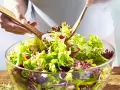 Frischer gemischter Salat mit knackigem Salat, Radieschen, Zwiebeln und Pilzen wird mit Holzsalatbesteck vermischt.