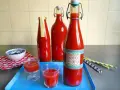 Rot gefüllte Flaschen mit dem Aufdruck "Mexikaner Rezept" und kleine Gläser mit dem Getränk.