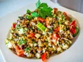 Frischer Linsensalat mit Feta, Paprika, Gurke und Kräutern, garniert mit Petersilie.