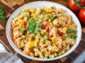 Bunter Couscous-Salat mit Tomaten, Paprika und Petersilie, garniert mit einem Petersilienblatt.