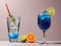 Zwei erfrischende Cocktails, einer blau, der andere klar mit blauen Akzenten, stehen neben frischen Früchten. Die Cocktail Bedeutung liegt im Genuss.