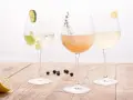 Drei elegante Gläser mit erfrischenden champagner cocktails, garniert mit Limette, Kräutern und Zitrone, stehen auf einem Holztisch.