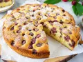 Ein saftiger, sommerlicher Kuchen mit Kirschen, bestäubt mit Puderzucker. Ein Stück wird gerade herausgeschnitten.