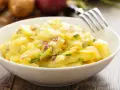 Ein cremiger Kartoffelsalat mit roten Zwiebeln und Schnittlauch in einer weißen Schüssel, bereit zum Genießen. Perfekt für ein Picknick oder als Beilage.