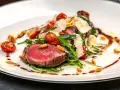 Saftiges Tagliata di Manzo mit Rucola, Kirschtomaten, Pinienkernen und Parmesan auf einem weißen Teller.