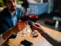 Drei Personen stoßen mit Rotwein an. Sie halten das weinglas richtig, am Stiel, um die Temperatur des Weins zu bewahren.