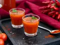 Zwei Gläser würziger mexikanischer Tomatensaft, garniert mit Petersilie, neben frischen Tomaten und Chilis.