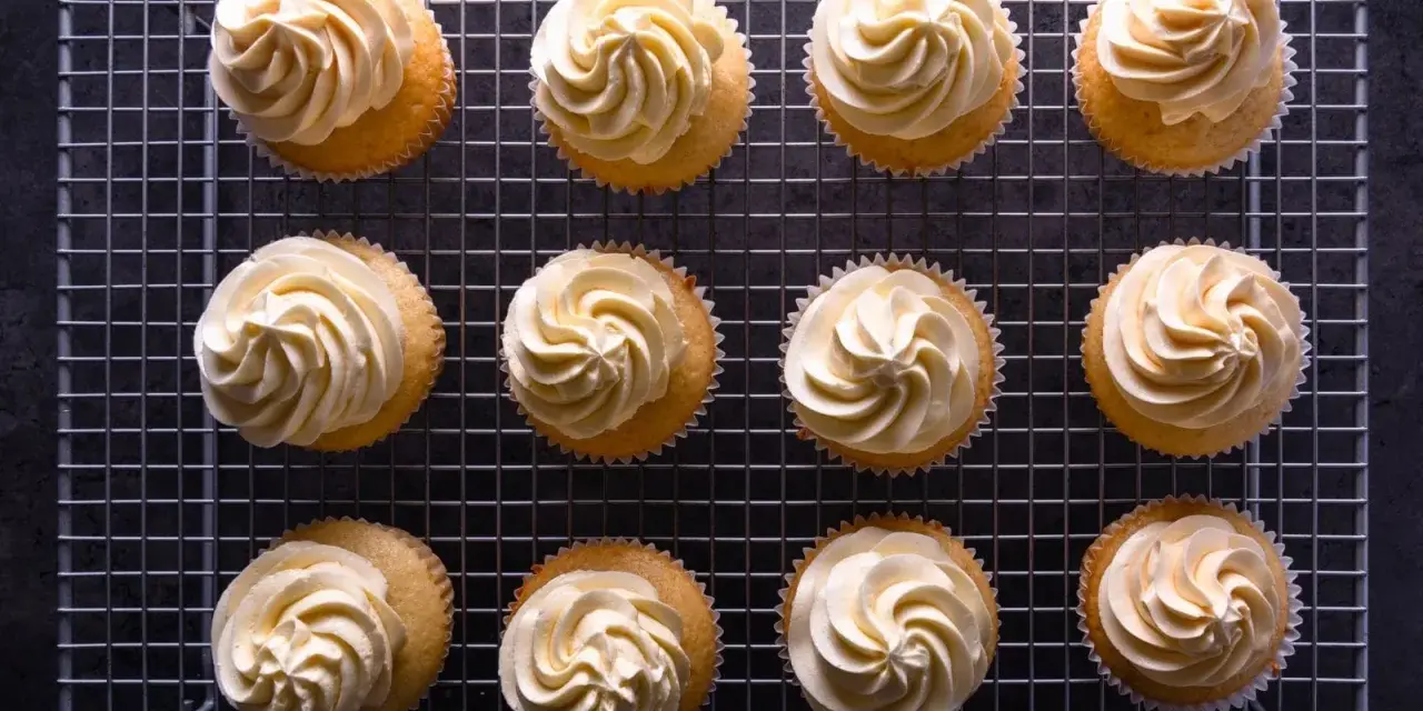 Zwölf Cupcakes mit cremiger deutscher Buttercreme auf einem Gitter.