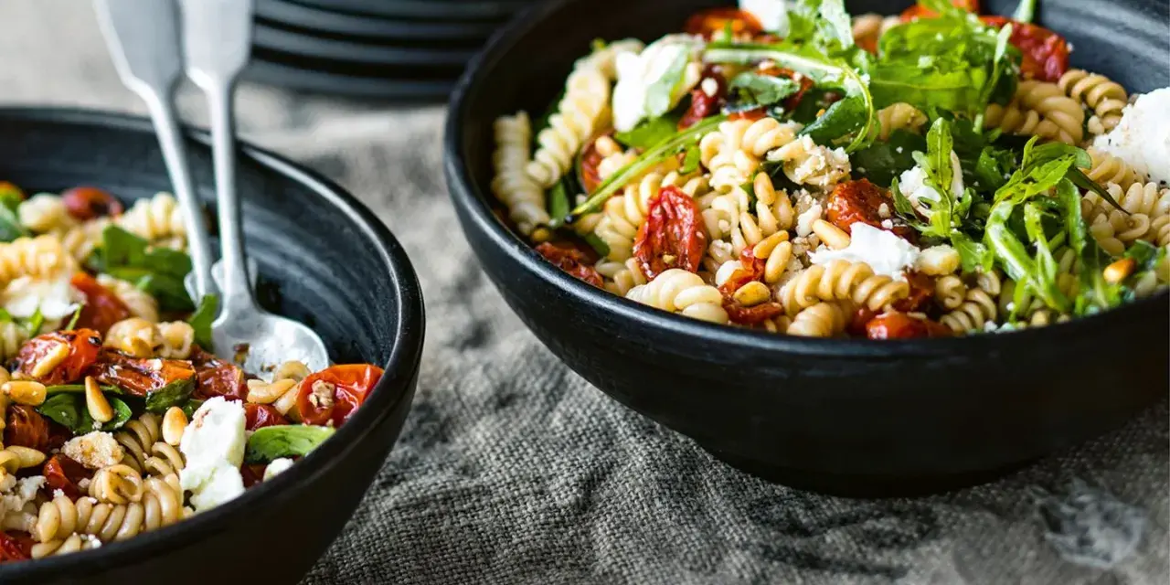 Zwei Schüsseln mit Nudelsalat, perfekt für das Grillen. Fusilli mit getrockneten Tomaten, Rucola und Feta.