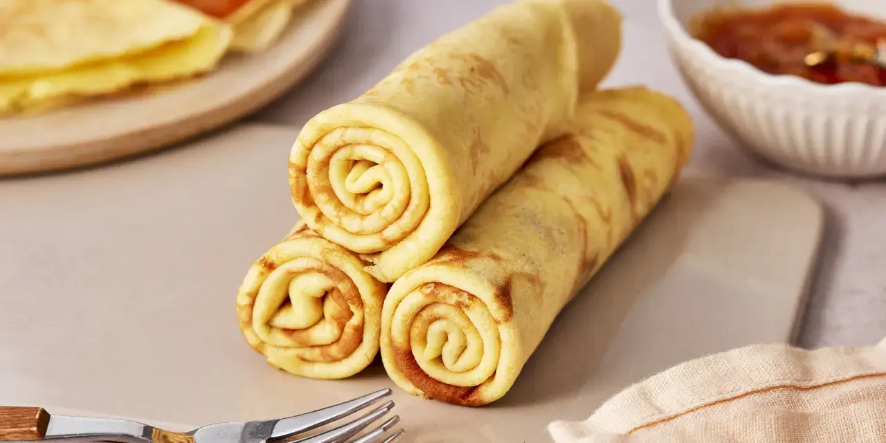 Gestapelte Quark Pfannkuchen, goldbraun gebacken, mit einer Schale Marmelade und Gabeln daneben.