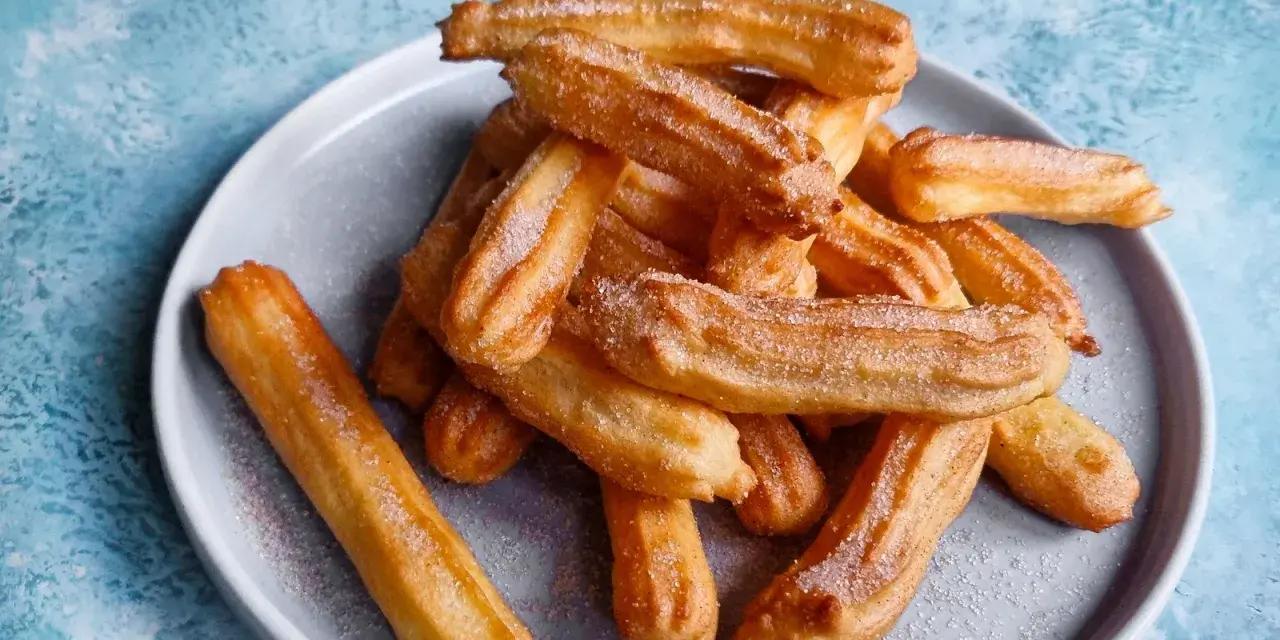 Goldbraune Churros, frisch aus dem Airfryer, mit Zucker bestreut auf einem grauen Teller.