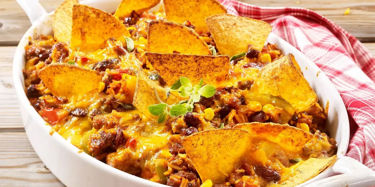 Herzhafter nacho auflauf mit Hackfleisch, Bohnen, Mais und geschmolzenem Käse, garniert mit Tortilla-Chips und frischen Kräutern.