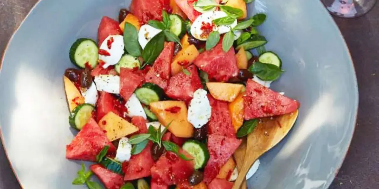 Erfrischender Melonensalat mit Mozzarella, Gurke und Basilikum auf einem grauen Teller.
