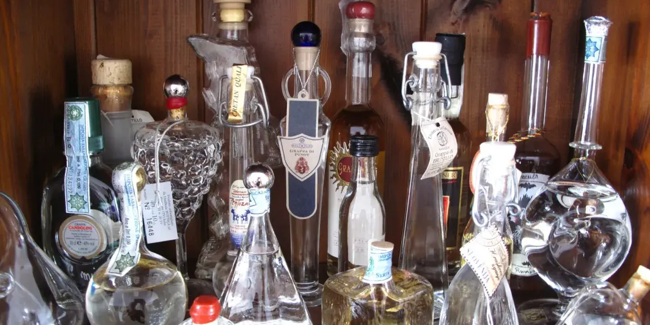 Regal voller Grappa-Flaschen, einige mit Etiketten, die den **Grappa Prozent** angeben.