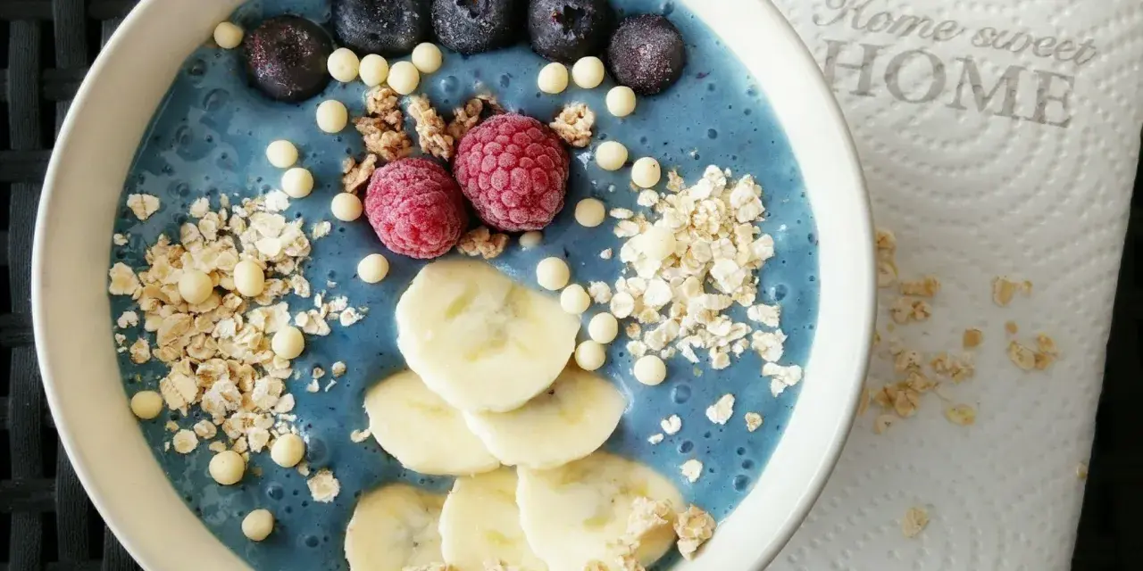 Blauer Smoothie-Bowl mit Blaubeeren, Himbeeren, Bananenscheiben und Granola. Perfekt für gesunde smoothie rezepte.