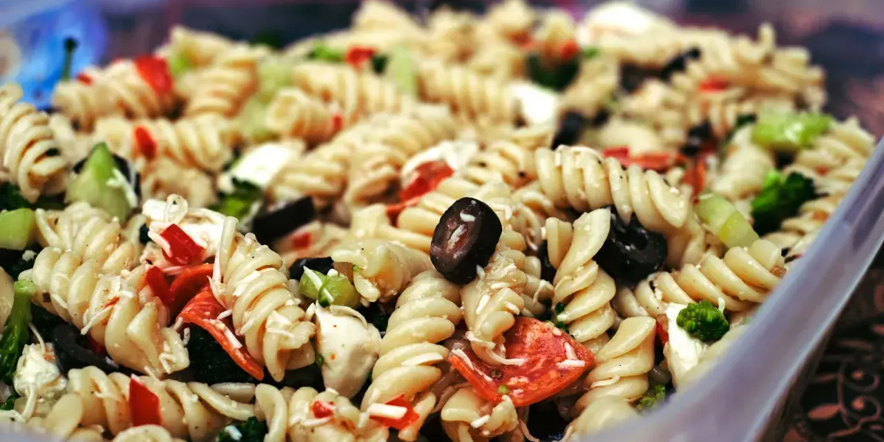 Nudelsalat mit Spiralnudeln, Oliven, Paprika und Brokkoli in einer Plastikschüssel.