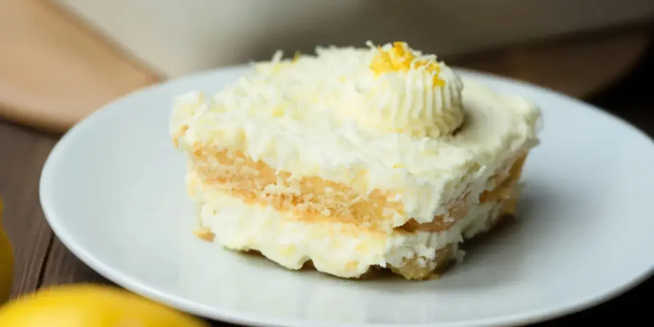 Ein Stück cremiges Limoncello Tiramisu, garniert mit Zitronenzesten und einem Tupfer Sahne, auf einem weißen Teller.