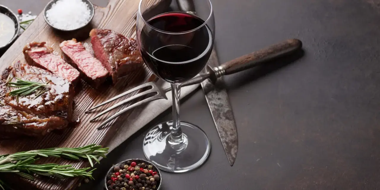 Ein saftiges Steak, perfekt zubereitet, mit einem Glas Rotwein. Was ist Malbec? Ein vollmundiger Wein, der dieses Gericht abrundet.