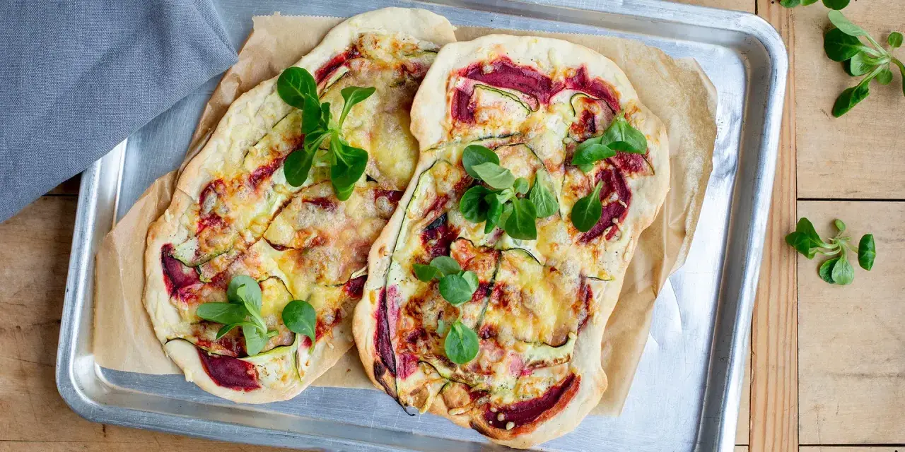 Zwei Flammkuchen mit Zucchini und Roter Bete, garniert mit frischen Blättern. Eine histaminarme Alternative, bei der man auf Weintrauben verzichtet.